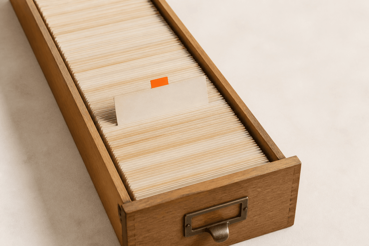 A long card-index drawer densely packed with plain filing cards, one card standing slightly proud with a small coral tab.
